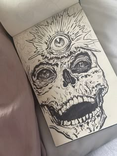 a drawing of a skull with an eye on it's forehead is laying on a bed