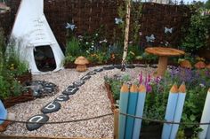 an outdoor garden with lots of plants and flowers on the ground next to a white teepee