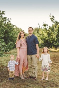 a man and woman with two children standing in an apple orchard, smiling at the camera