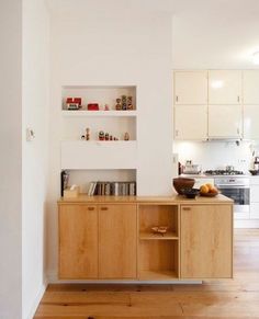 a kitchen with white walls and wooden floors is shown in this image, there are shelves on the wall