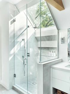 a bathroom with a walk in shower next to a white sink and counter top under a skylight