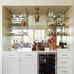 a kitchen with white cabinets and gold shelves filled with bottles, glasses, and liquor