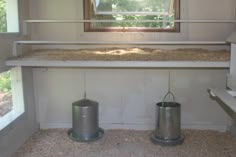 two metal trash cans sitting on top of a shelf next to a window in a room