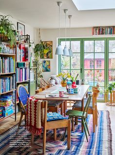 a dining room table with chairs and bookshelves in front of large open windows