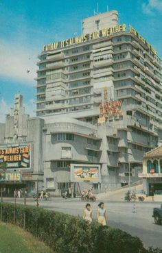 people walking in front of a tall building on the corner of a street with cars driving by