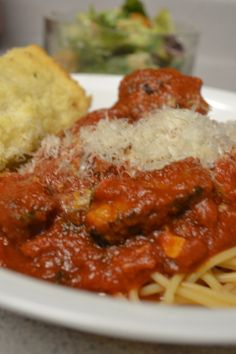 a white plate topped with spaghetti and meatballs covered in sauce next to bread on top of a table