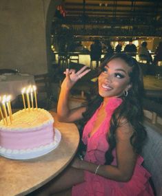 a woman sitting in front of a pink cake with candles on it and smiling at the camera