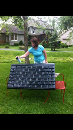 a woman in blue shirt standing next to a black keyboard on grass with trees and houses behind her