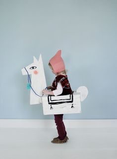 a young child is dressed up as a horse and holding a paper mache with a pink hat on it's head