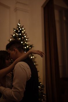 a man and woman standing in front of a christmas tree with their arms around each other