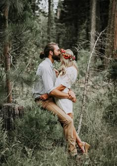 a man and woman kissing in the woods with pine trees behind them, surrounded by tall grass