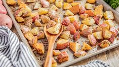 potatoes and broccoli on a baking sheet with a wooden spoon next to them