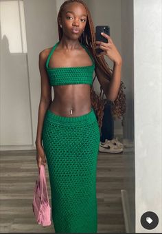 a woman taking a selfie with her cell phone wearing a green crop top and matching skirt