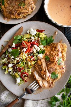 two plates with chicken, salad and gravy next to a bowl of sauce