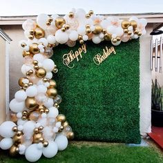 a balloon arch with happy birthday balloons on it in front of a green wall and potted plant