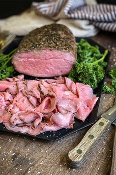 some meat and broccoli on a black plate next to a pair of knives