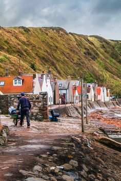 there is a man walking down the street in front of some houses and water with mountains behind him