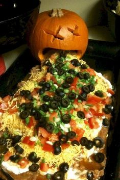 a halloween pizza with black olives, tomatoes and cheese on it next to a jack - o'- lantern