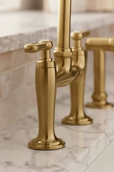 three golden faucets sitting on top of a marble counter