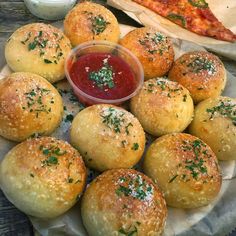 bread rolls are arranged on a plate with dipping sauce and two pizzas in the background