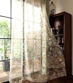 an open window with sheer curtains in front of a wooden shelf and potted plant