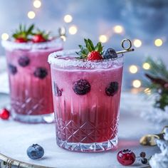 two glasses filled with ice and berries on top of a white tray next to christmas decorations