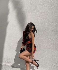 a woman leaning against a white wall with her legs crossed and wearing high heeled shoes