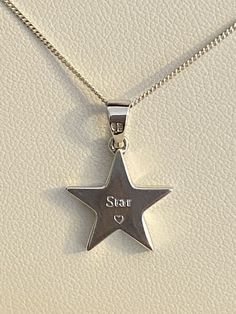 a silver star pendant with the word star on it's side hanging from a chain