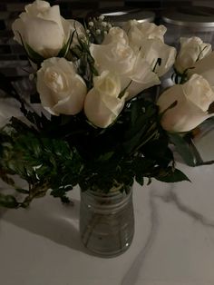 a vase filled with white roses sitting on top of a marble countertop next to a sink