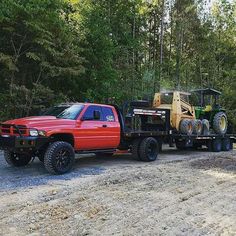 a red truck with two large tractors on it's flatbed is parked in front of some trees