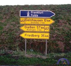 a bunch of street signs sitting on the side of a road next to a grass covered hill