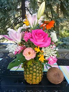 a pineapple vase filled with colorful flowers on top of a table next to a coconut