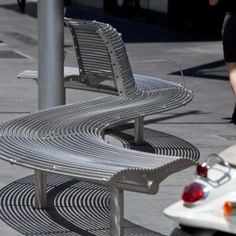 two metal benches sitting next to each other on a sidewalk near a scooter