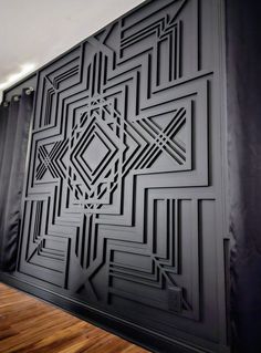 a black and white wall with an intricate design on the back side, along with wooden flooring