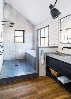 a bathroom with white brick walls and wood flooring is pictured in this image, there are two mirrors on the wall above the bathtub