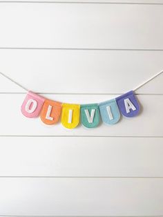 the word ollivia spelled in multicolored letters hanging from a string on a white wall