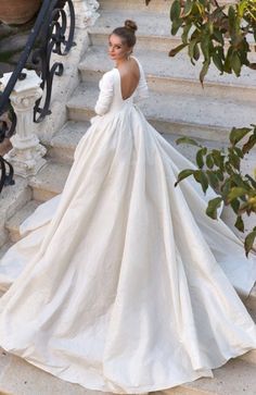 a woman in a wedding dress walking up some stairs with her back turned to the camera