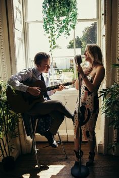 a man and woman playing guitar in front of a window