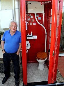 a man standing in front of a red phone booth next to a toilet and sink