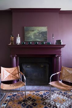 two chairs sitting in front of a fire place with a painting on the wall behind them