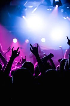 a crowd of people at a concert with their hands up in the air and lights on