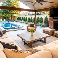 an outdoor living area with couches, tables and a television on the wall next to a swimming pool