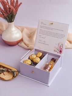 an open box with some chocolates in it on a table next to a vase