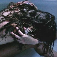 a woman with wet hair in a bathtub holding her hands to her head and looking down