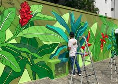 a man painting a mural on the side of a building with flowers and leaves painted on it