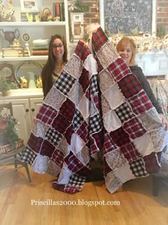 two women standing next to each other in front of a large piece of quilts