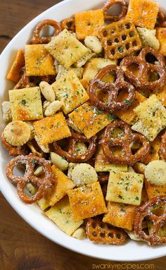 a white bowl filled with cheesy crackers and pretzels on top of a wooden table