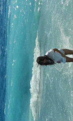 a woman standing on top of a surfboard in the ocean next to a wave