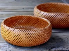 two brown woven baskets sitting on top of a wooden table next to each other,