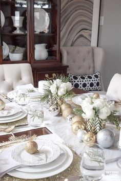 a dining room table set for christmas with white and gold decorations